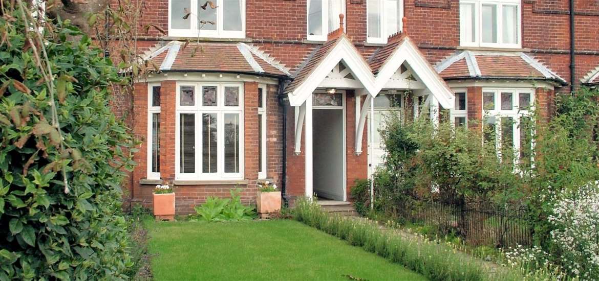 Image description: A red brick house with white windows, 6 The Terrace, with grassed front garden