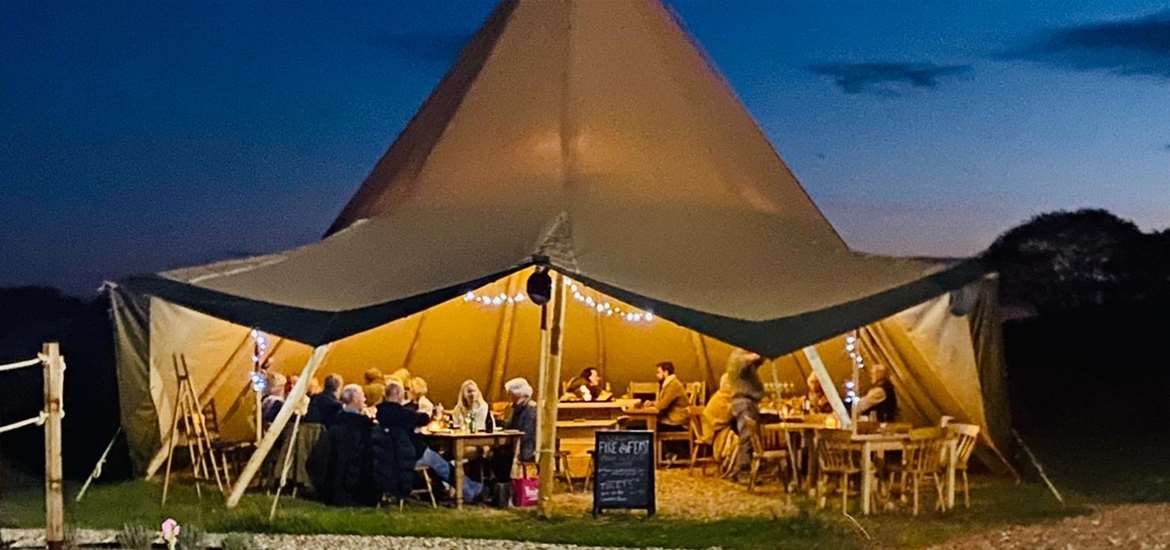 Fire and feast - tipi at night with people eating dinner inside